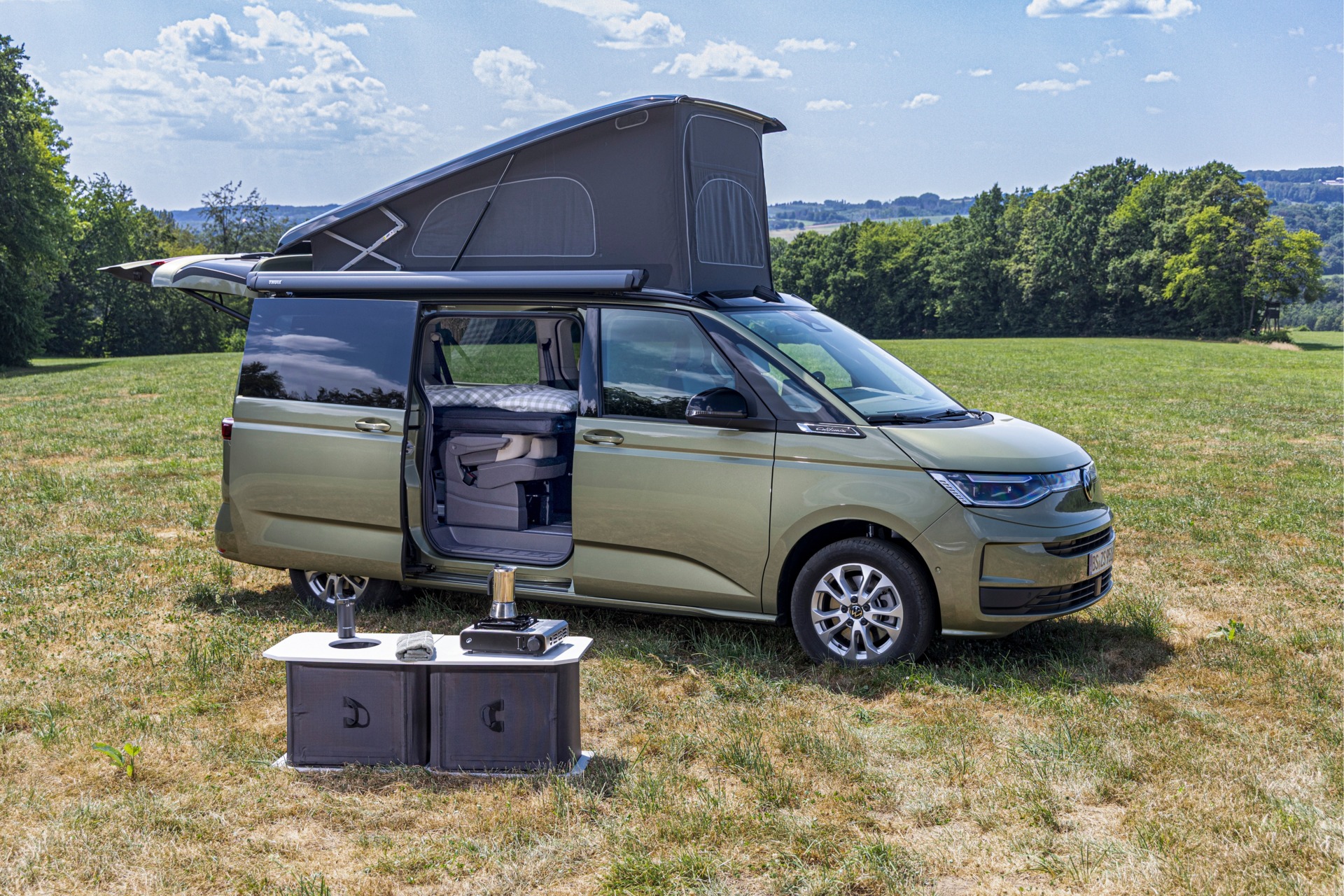 Wohnmobil California mit aufgestelltem Dach und offener Schiebetür auf einer Wiese