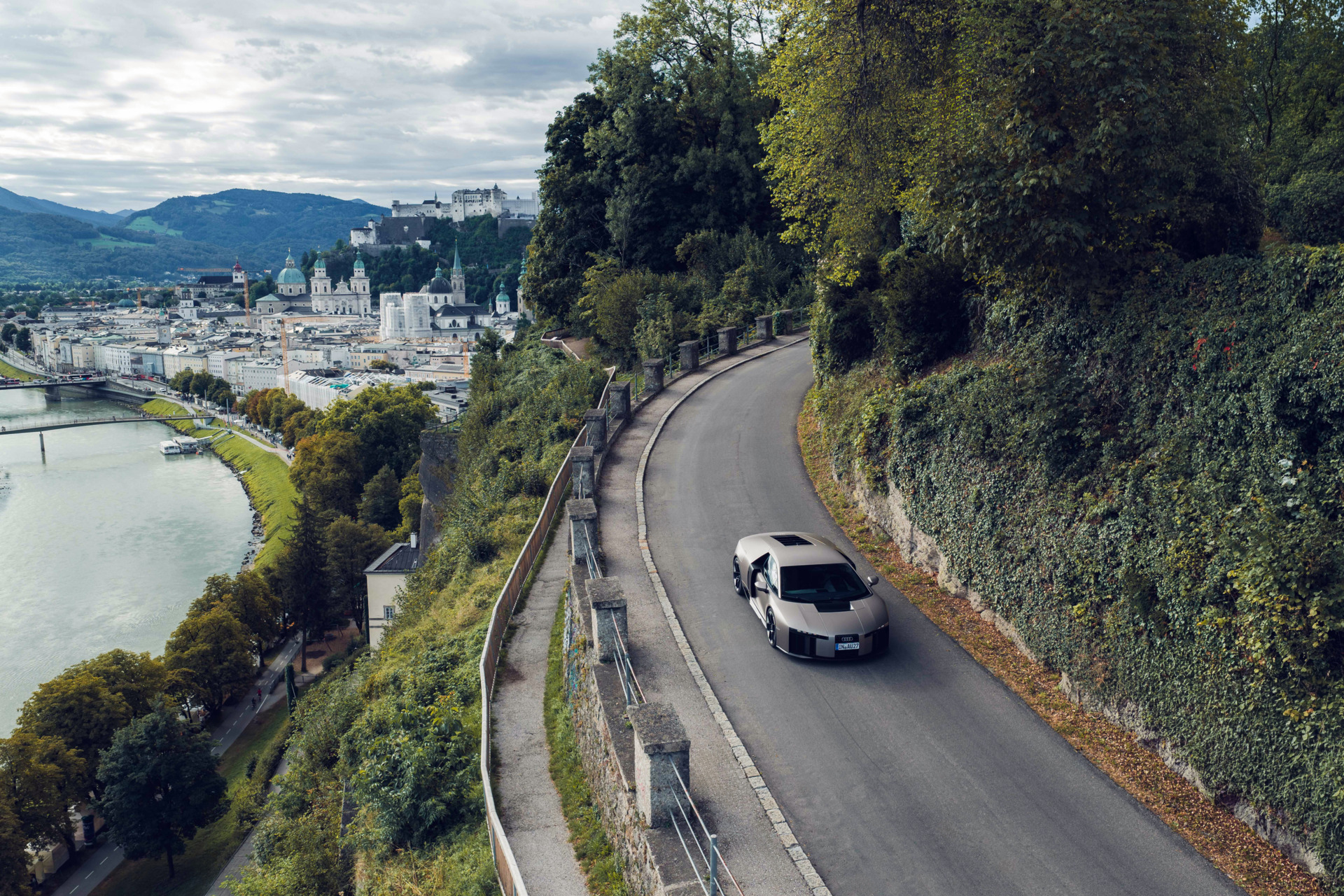 Silberner Sportwagen fährt auf kurviger Straße mit Blick auf Salzburg und Festung Hohensalzburg.
