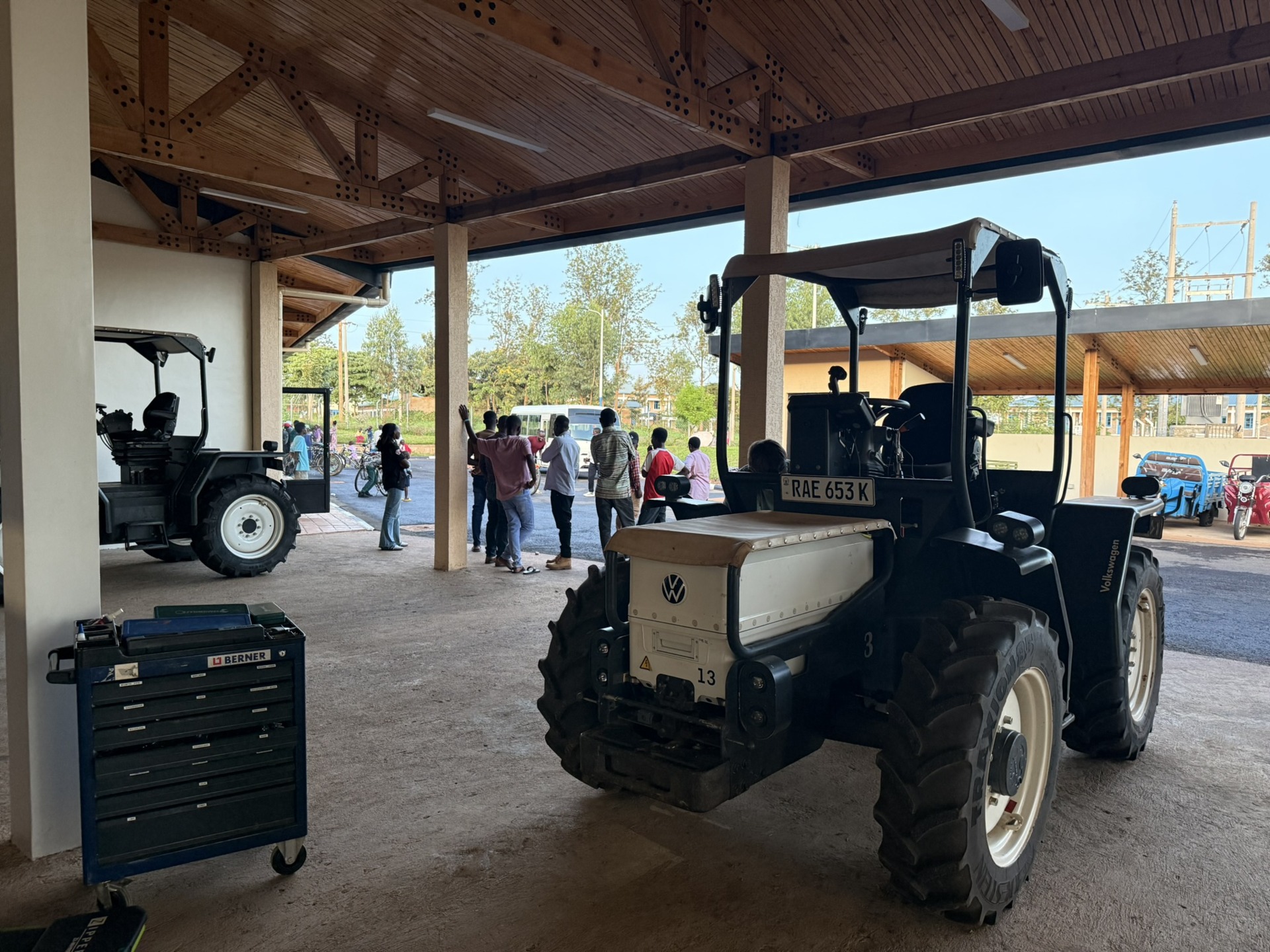 Traktor mit Nummerntafel RAE 653 K vor Menschengruppe und Werkzeugwagen